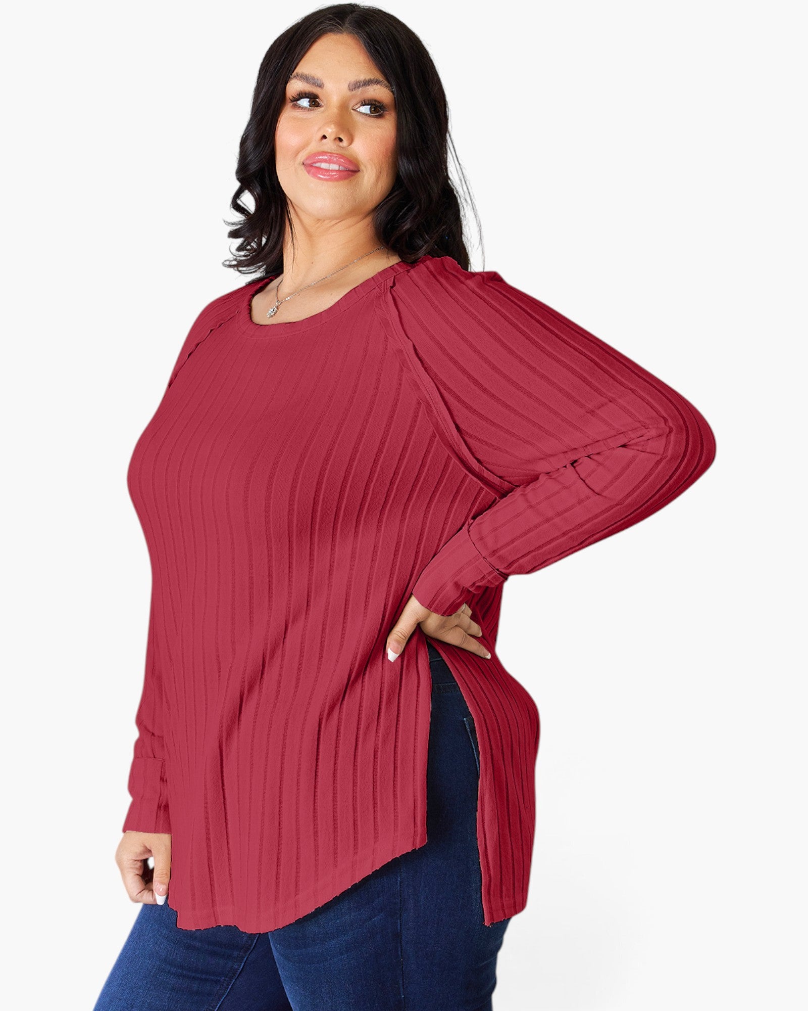 A woman modeling a ribbed long-sleeve top in a deep berry red color, paired with dark blue jeans, against a plain white background.