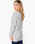A woman with blonde hair is shown from a side-back angle wearing a light gray ribbed knit long-sleeve top and dark blue jeans against a plain white background.
