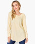 A woman wearing a pale yellow long-sleeve ribbed knit tunic top with blue jeans, photographed against a plain light gray studio background.
