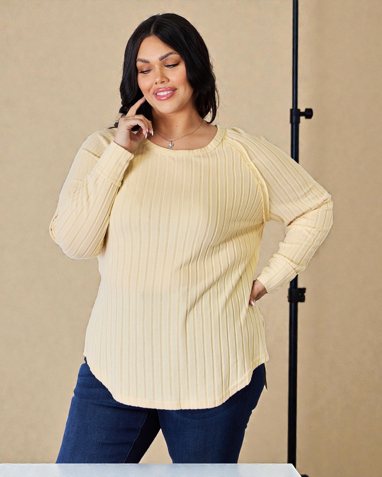 Woman wearing a yellow ribbed sweater and blue jeans against a beige background