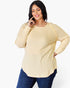 A woman wearing a cream-colored ribbed long-sleeve top and dark blue jeans, posing against a solid white background.