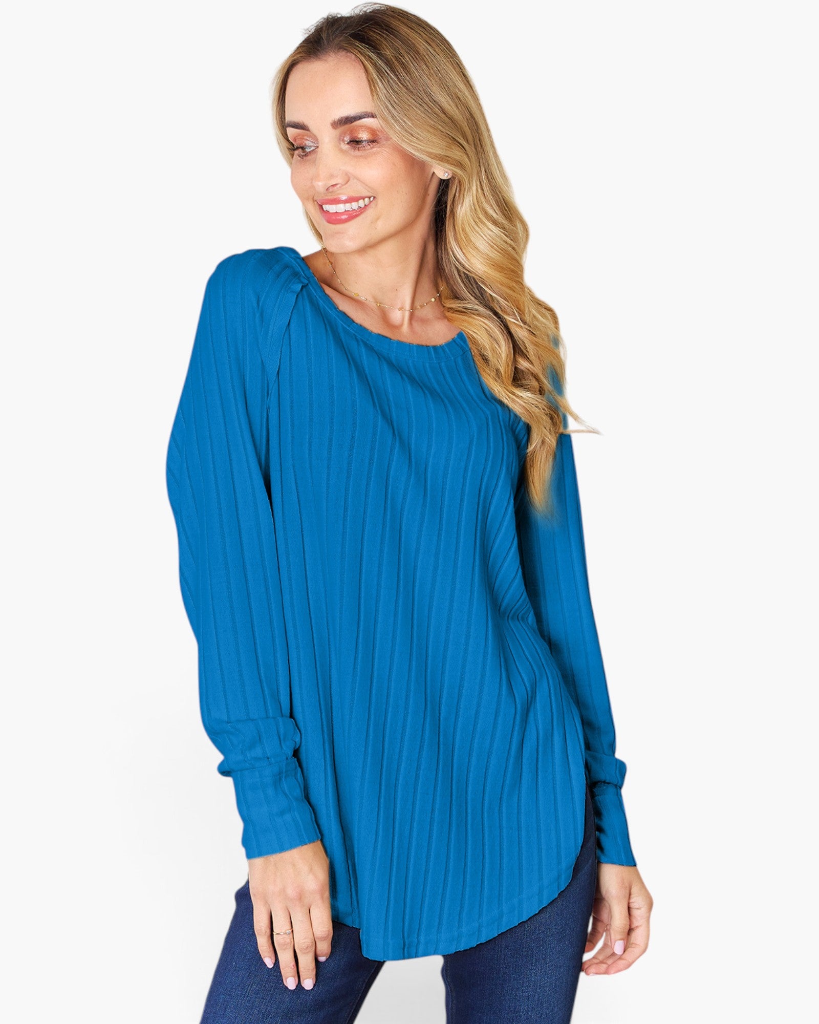 A woman wearing a bright blue long-sleeve top with a vertical pleated texture, paired with dark blue jeans, against a plain white background.