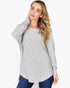 A woman wearing a light gray ribbed knit long-sleeve tunic top with blue jeans, posing against a solid white studio background.