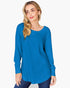 A woman modeling a bright blue long-sleeve ribbed knit top with a wide scoop neckline, paired with dark blue jeans, against a plain light gray background.