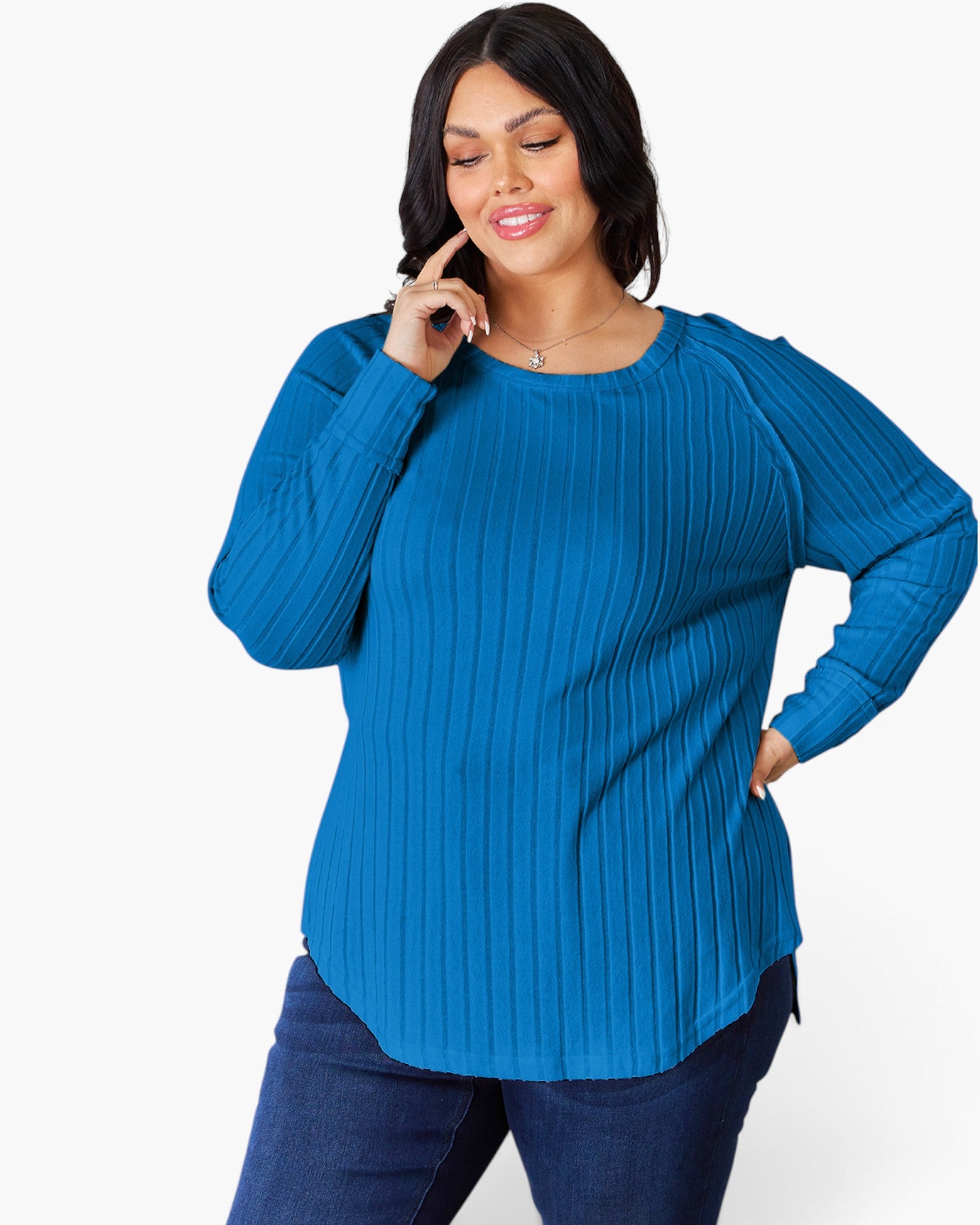 A woman modeling a bright blue ribbed knit long-sleeve top with a crew neck, paired with dark blue jeans, against a plain white studio background.