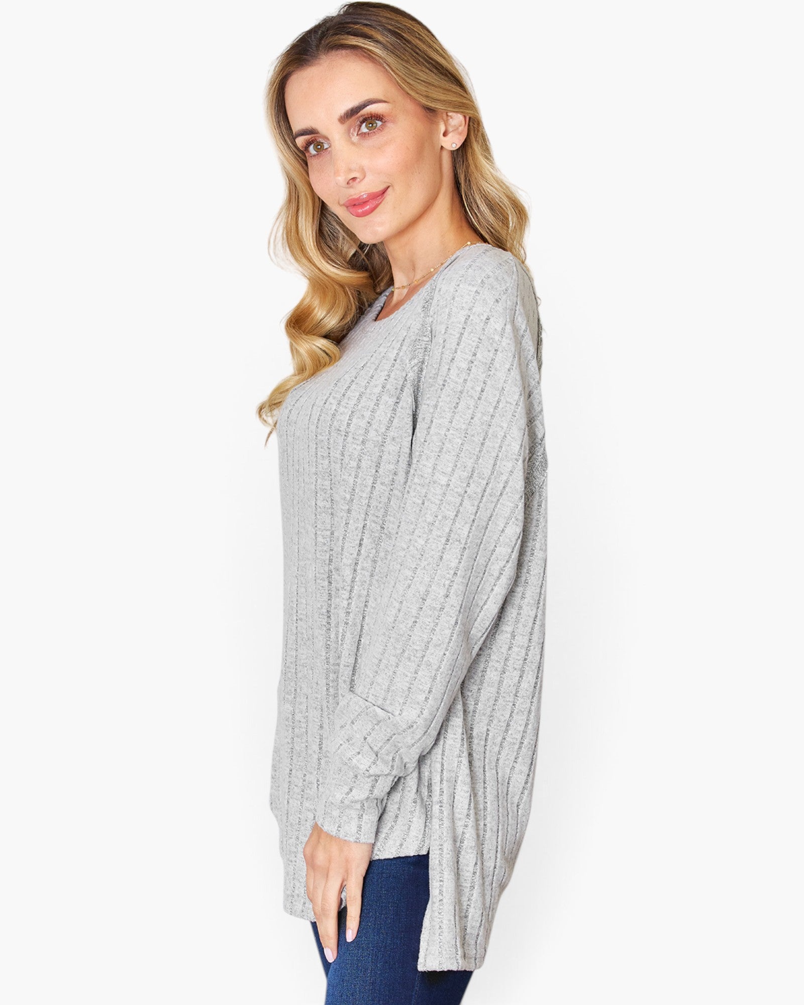 A woman modeling a light gray ribbed knit long-sleeve top with a crew neckline, paired with blue jeans, against a plain white background.