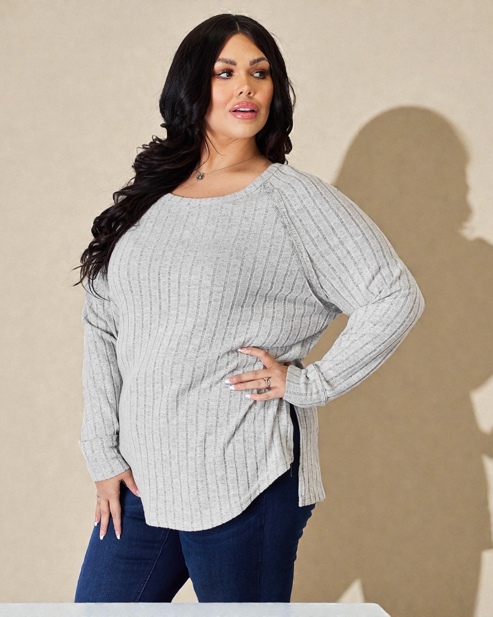 Woman wearing a gray ribbed sweater and blue jeans against a beige background