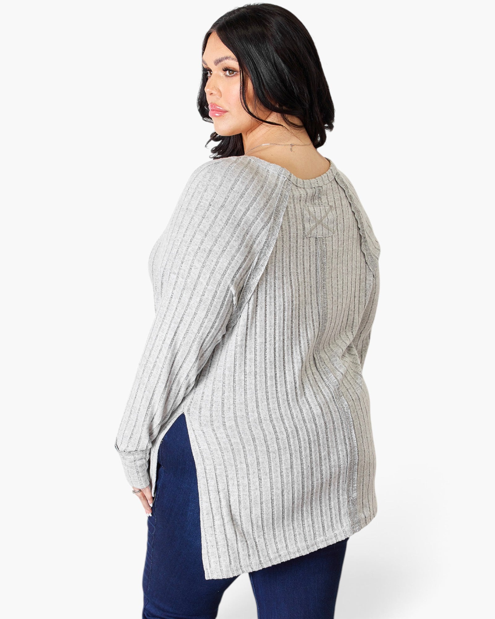 A woman modeling a light gray ribbed knit long-sleeve top from the back, paired with dark blue jeans, against a plain white background.