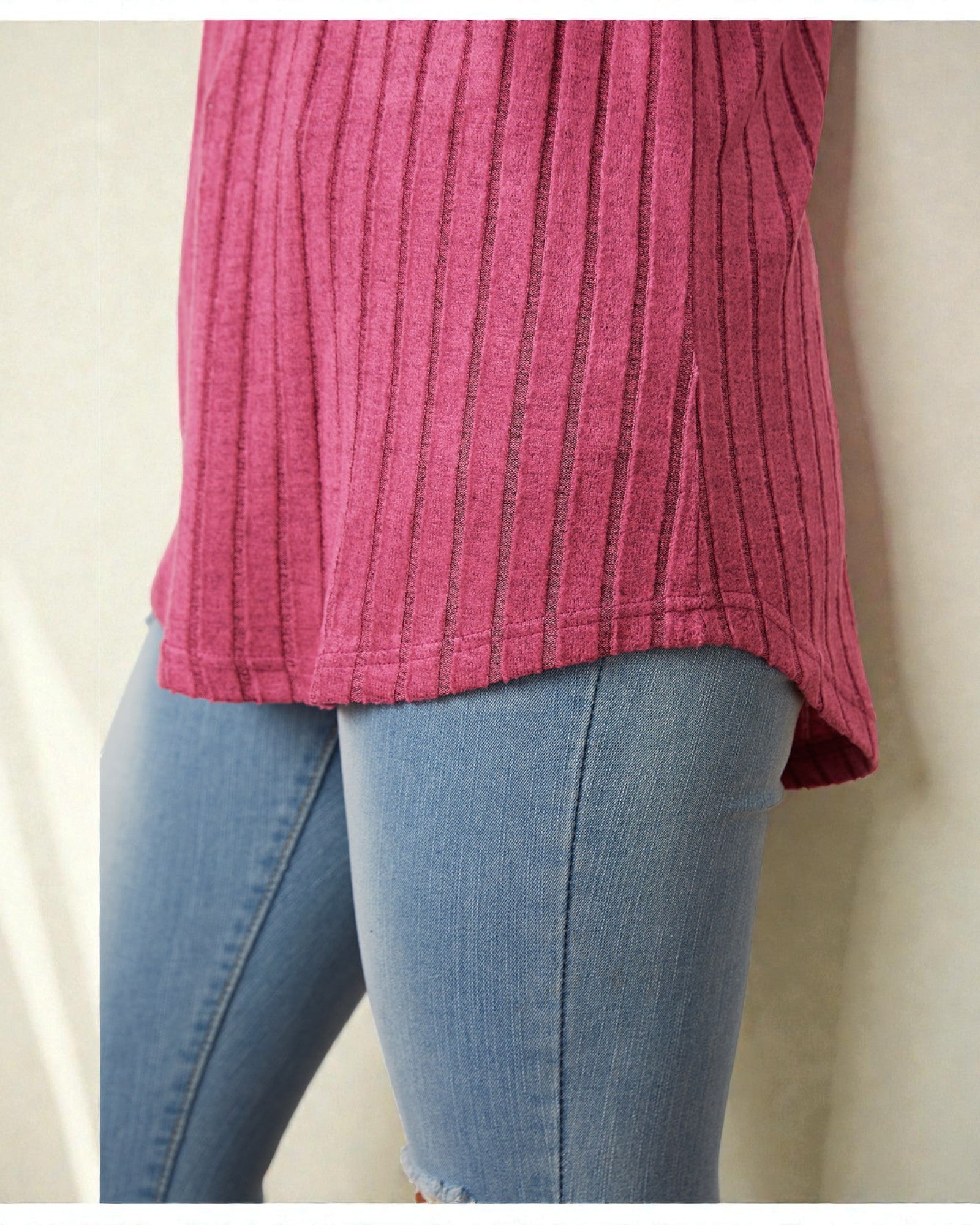 Person wearing a pink textured top and blue jeans on a beige background
