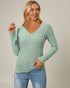 Woman wearing a green ribbed sweater and blue jeans against a plain background