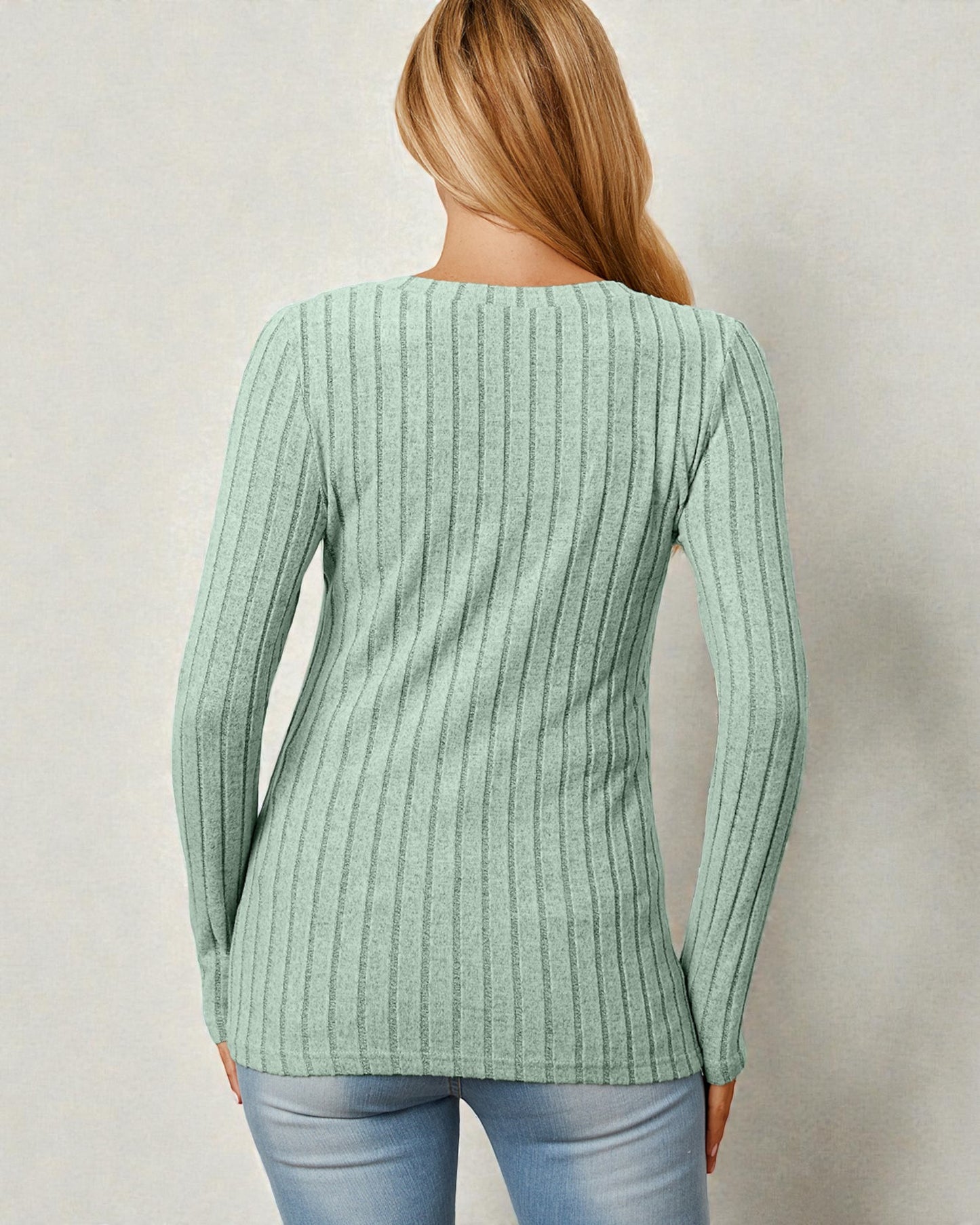 Person wearing a green ribbed sweater against a plain background
