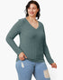 A woman modeling a ribbed long-sleeve V-neck sweater in a muted sage green color, paired with light blue distressed jeans, against a plain white background.