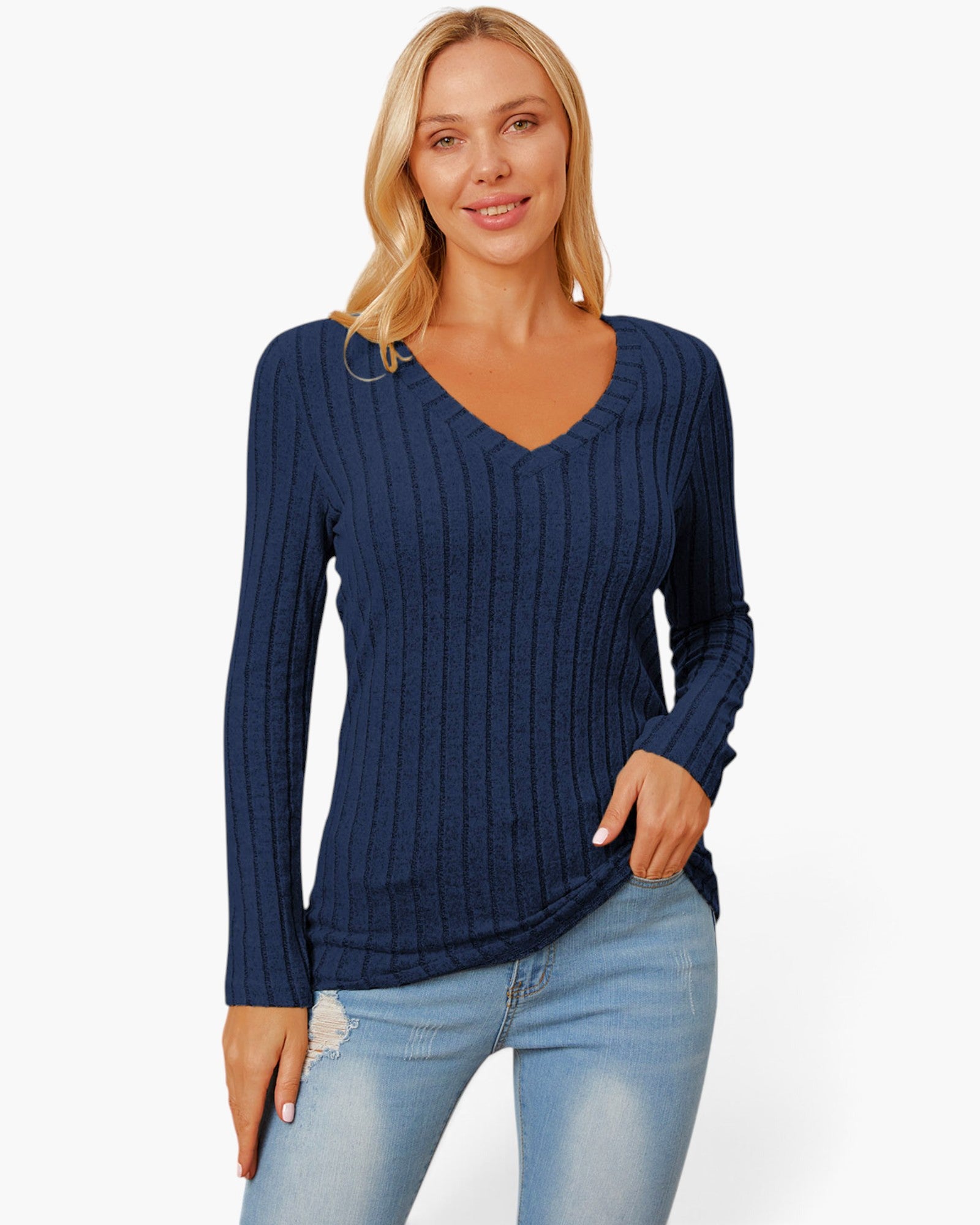 A woman wearing a navy blue ribbed long-sleeve V-neck sweater and light blue jeans, standing against a plain white studio background.