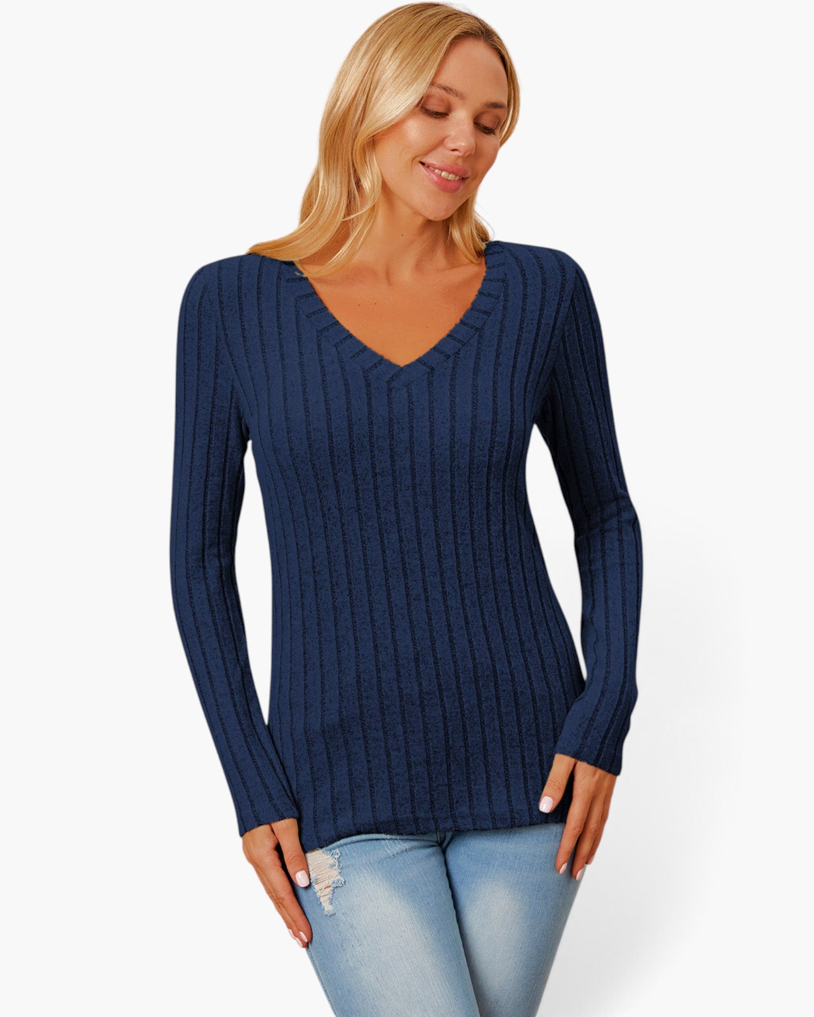 A woman wearing a navy blue ribbed long-sleeve V-neck sweater and light blue jeans, standing against a plain white studio background.