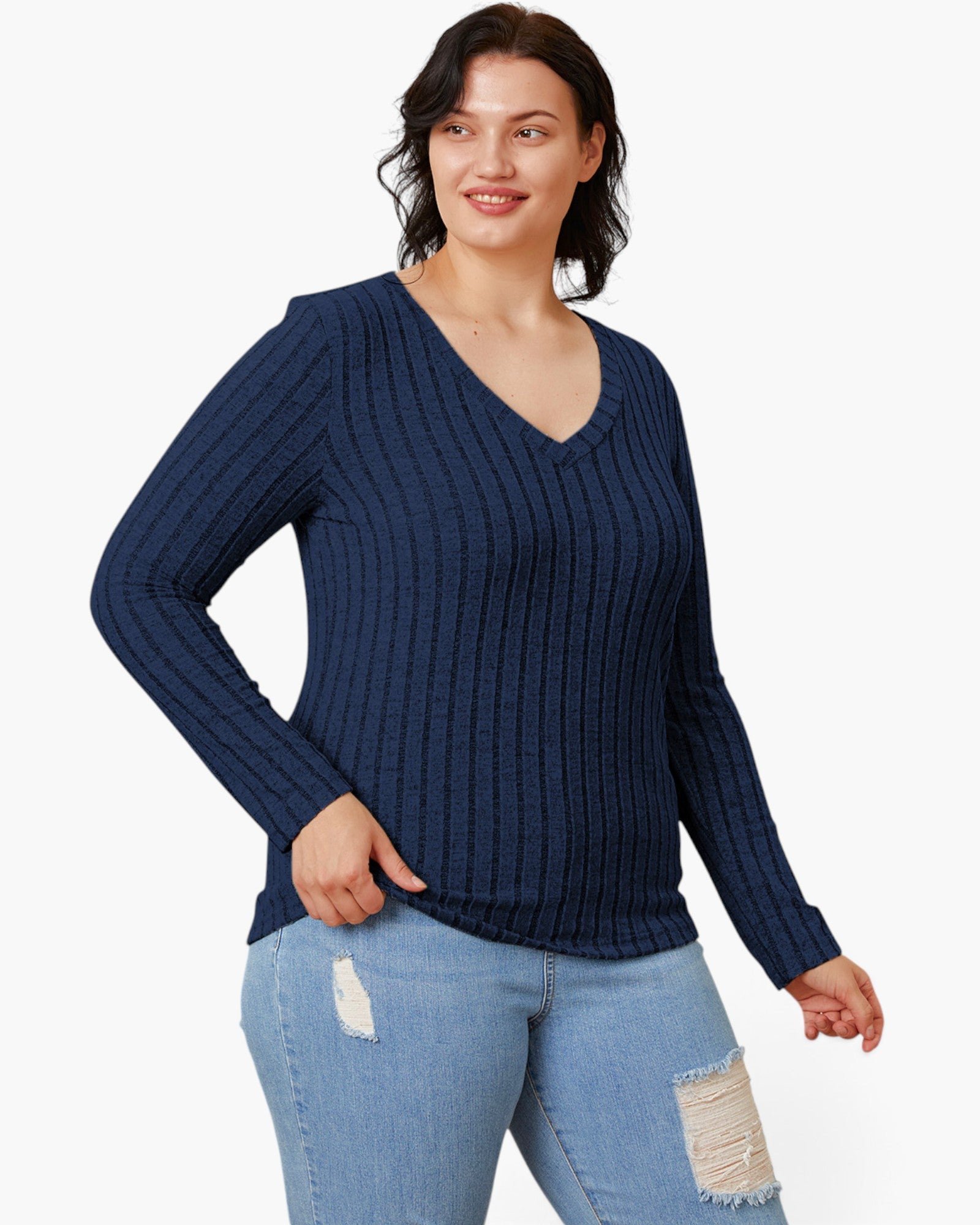 A woman wearing a navy blue ribbed long-sleeve V-neck sweater and light blue distressed jeans, standing against a plain white studio background.