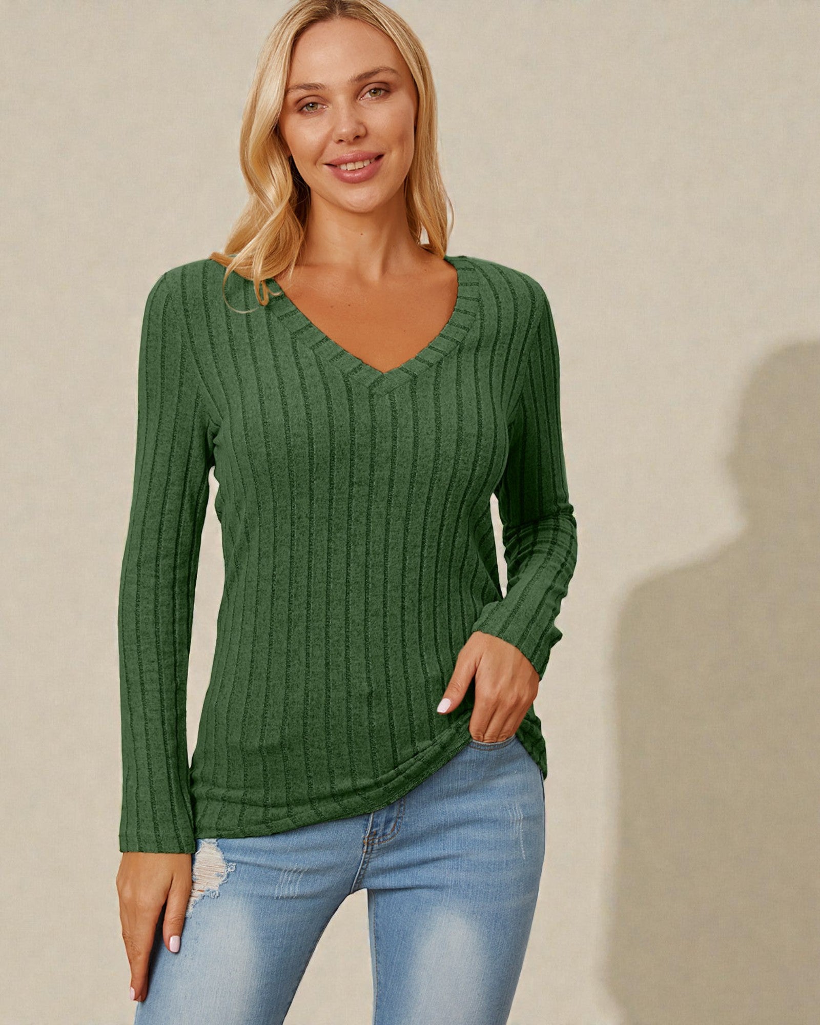 Woman wearing a green sweater and blue jeans against a beige background