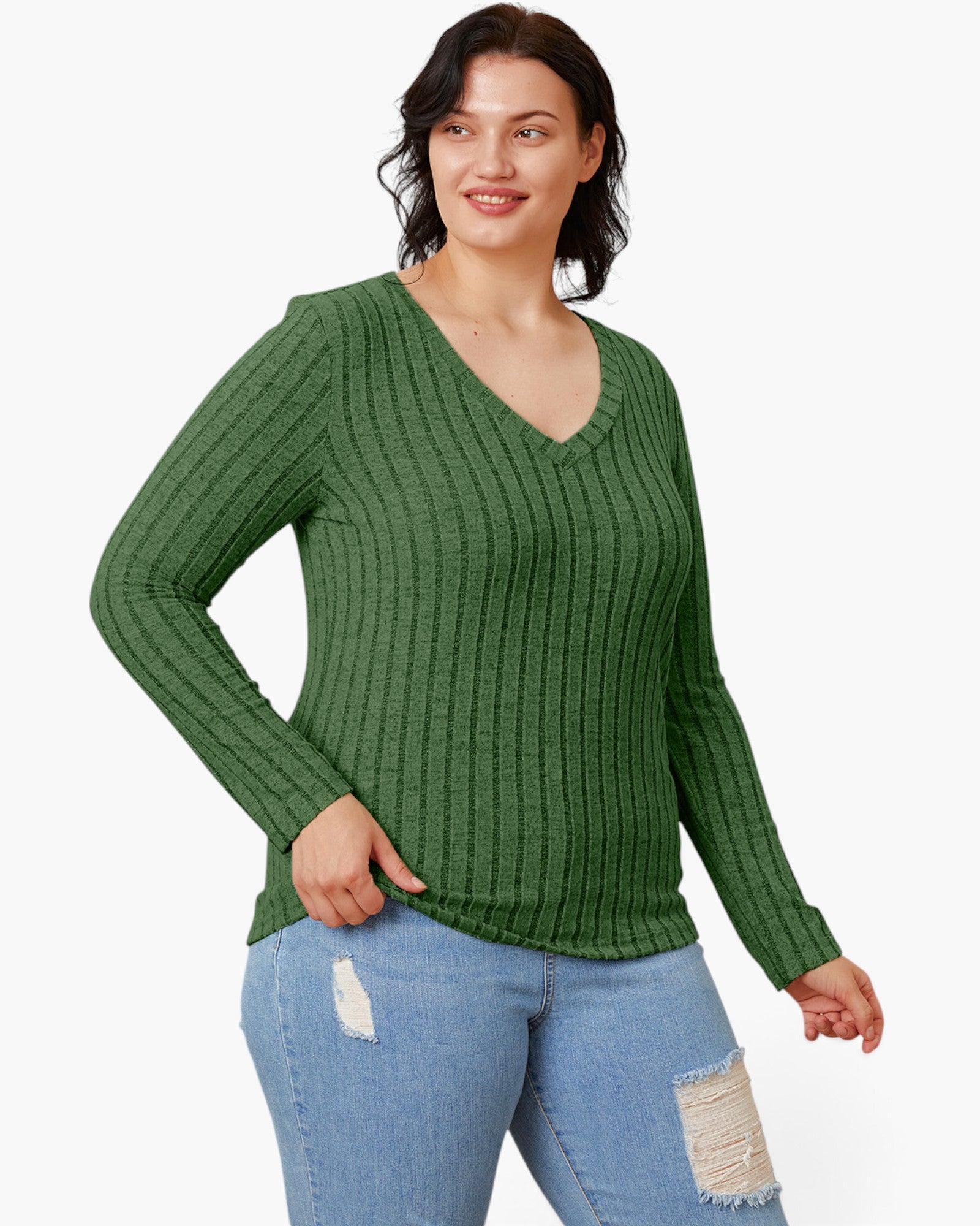 A woman wearing a green ribbed long-sleeve V-neck sweater and light blue distressed jeans, standing against a plain white studio background.