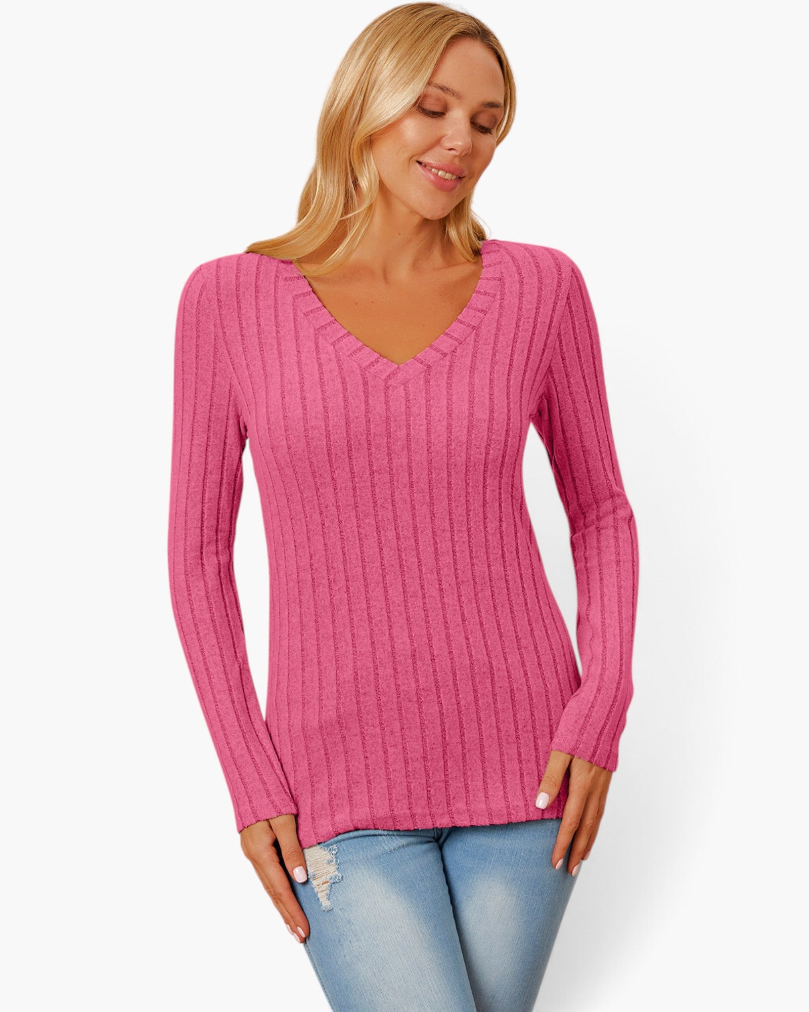 A woman wearing a pink ribbed long-sleeve V-neck sweater and light blue jeans, standing against a plain white studio background.