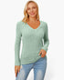 A woman modeling a sage green ribbed knit long-sleeve V-neck sweater with light blue jeans against a plain white studio background.