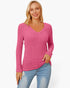 A woman wearing a pink ribbed long-sleeve V-neck sweater and light blue jeans, standing against a plain white studio background.