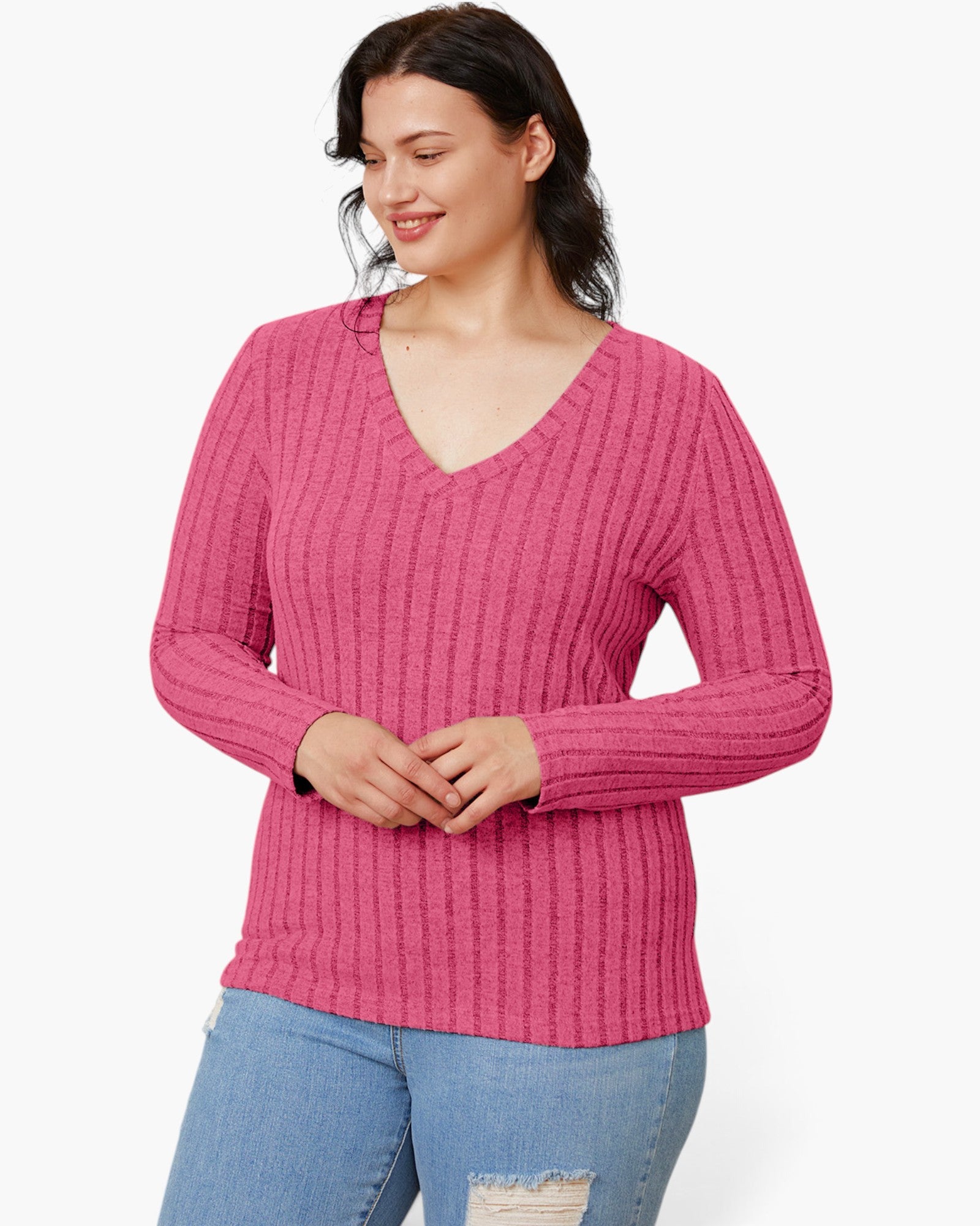 A woman wearing a pink ribbed long-sleeve V-neck sweater and light blue jeans, standing against a plain white studio background.