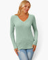A woman wearing a sage green ribbed long-sleeve V-neck sweater and light blue jeans, standing against a plain white studio background.