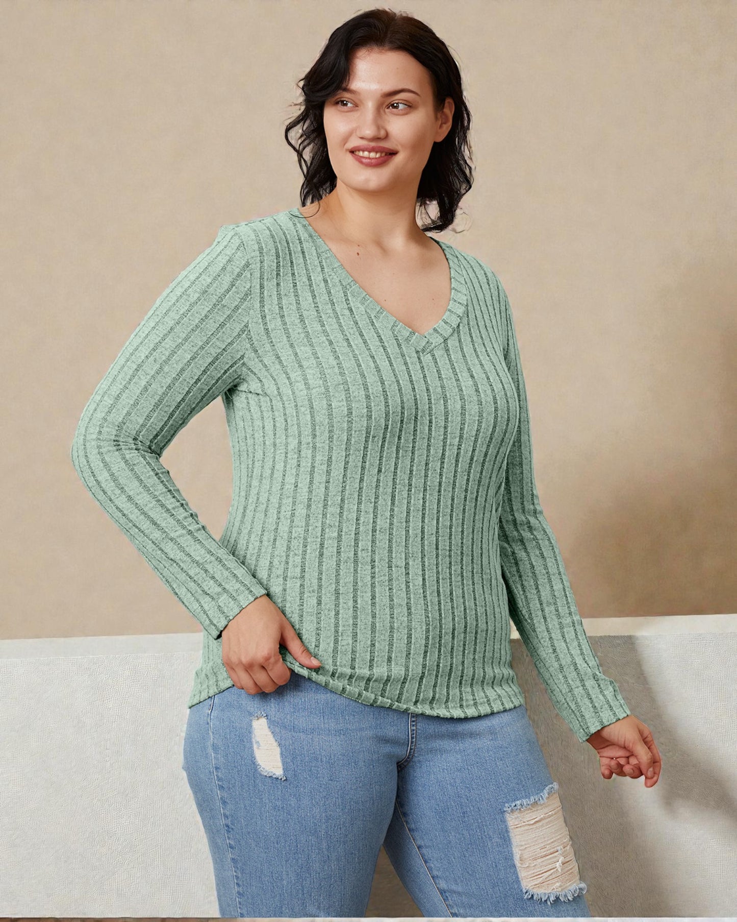 Woman wearing a green ribbed sweater and blue jeans against a beige background