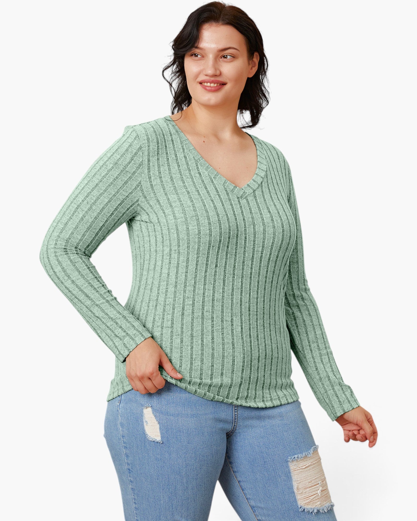 A woman modeling a light sage green ribbed knit long-sleeve V-neck sweater with light blue distressed jeans against a plain white background.