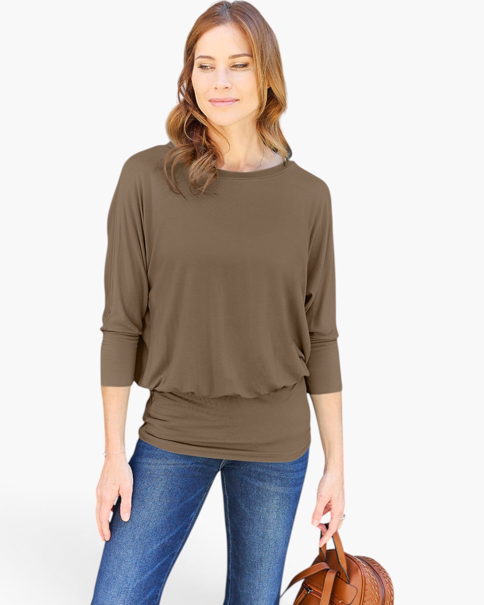 A woman wearing a brown three-quarter sleeve top with a ruffled hem, paired with blue jeans and holding a brown leather handbag, set against a plain white background.
