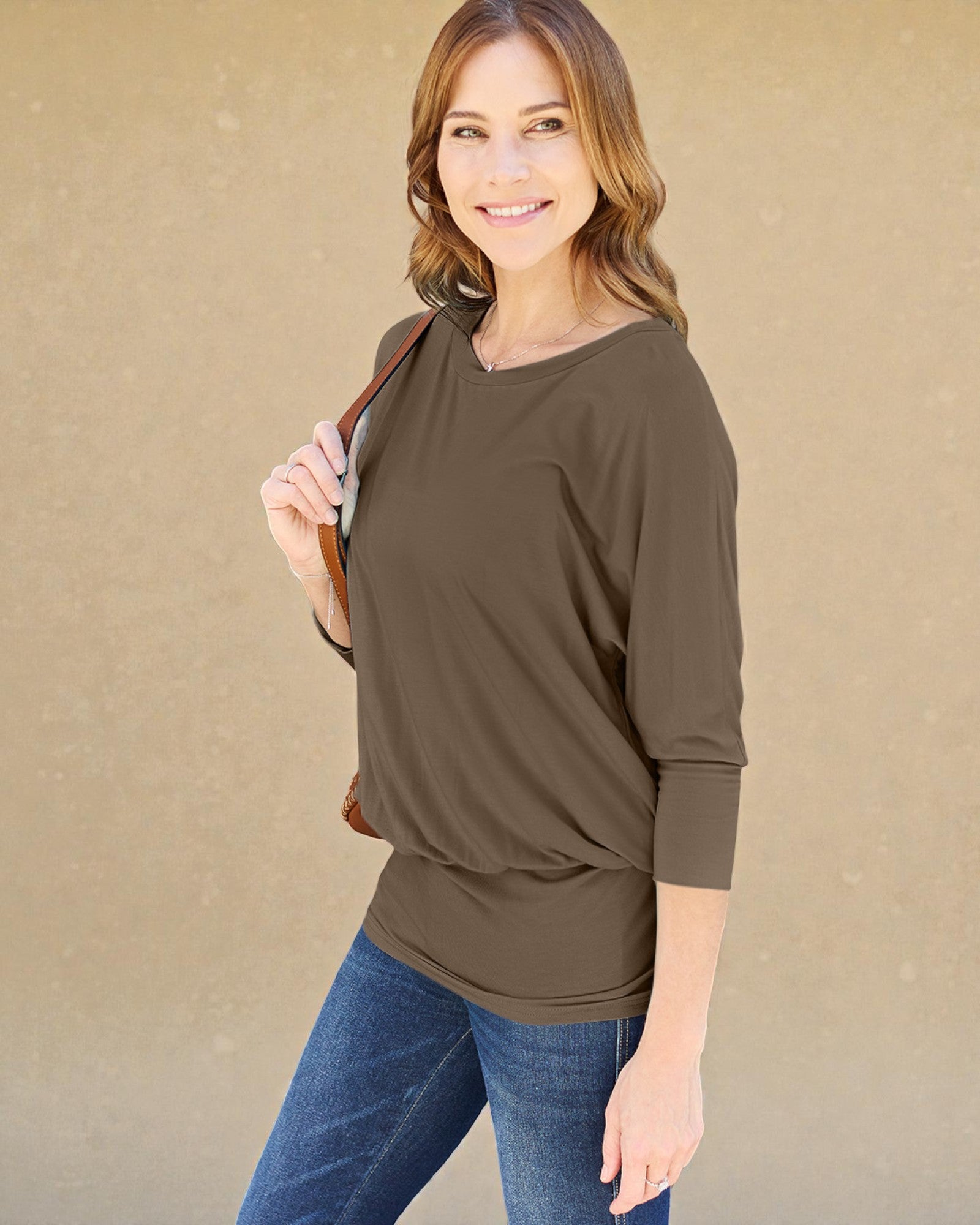 Woman wearing a brown long-sleeve top and blue jeans against a beige background
