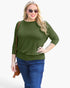 A woman modeling a three-quarter sleeve olive green top with a crew neck, paired with blue jeans and a small brown crossbody bag, against a plain white background.