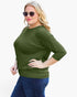 A woman modeling a three-quarter sleeve olive green top with a boat neckline, paired with blue jeans, against a plain white background.