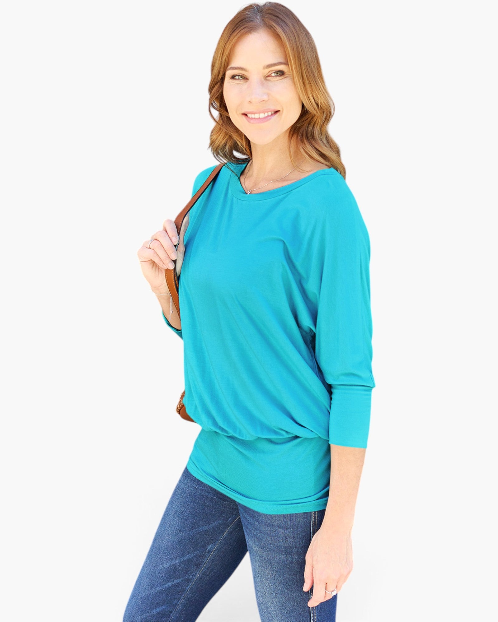 A woman modeling a bright turquoise blue long-sleeve top with a relaxed, slightly draped fit, paired with blue jeans against a plain white background.