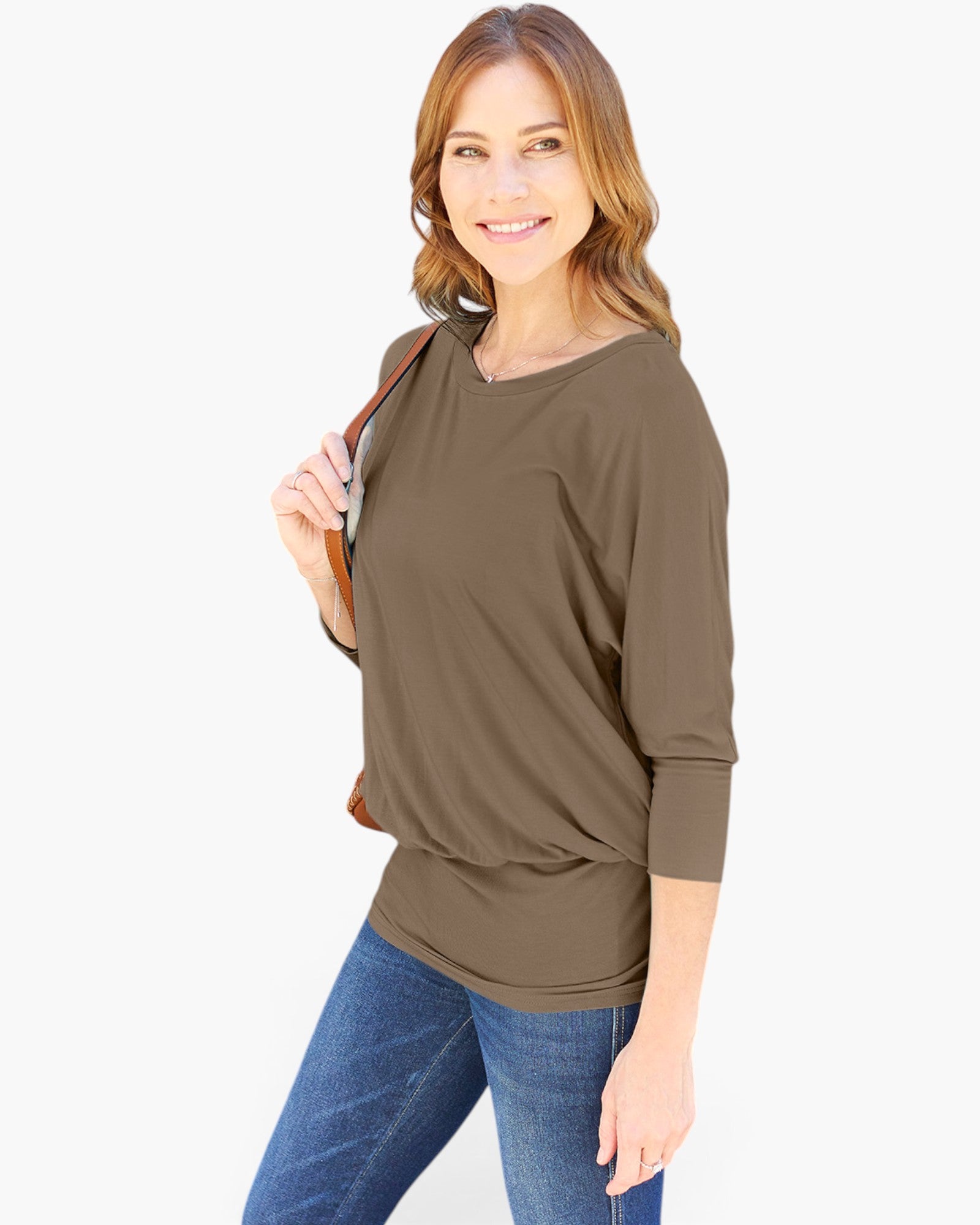 A woman modeling a brown three-quarter sleeve top with a relaxed, slightly draped silhouette, paired with blue jeans and holding a brown shoulder bag against a plain white background.
