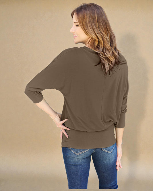 Woman wearing a brown long-sleeve top and blue jeans against a beige background