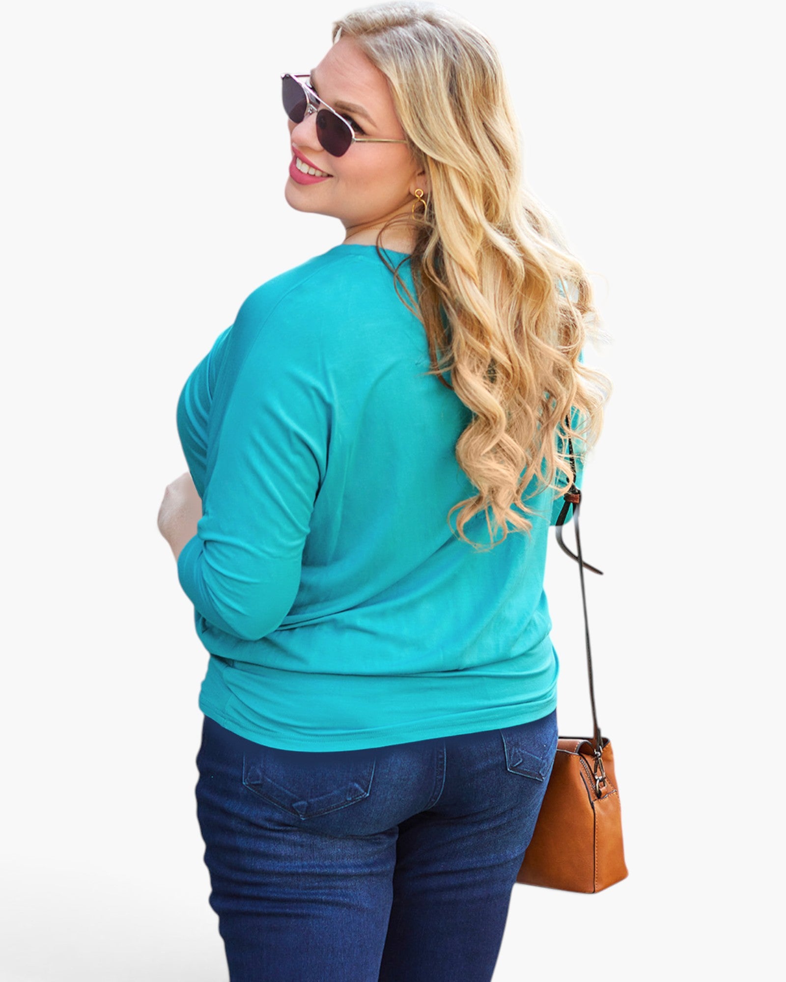 A woman with long blonde hair, wearing sunglasses, a bright teal long-sleeve top, and dark blue jeans, shown from a back-three-quarter angle while carrying a brown leather shoulder bag against a plain white background.