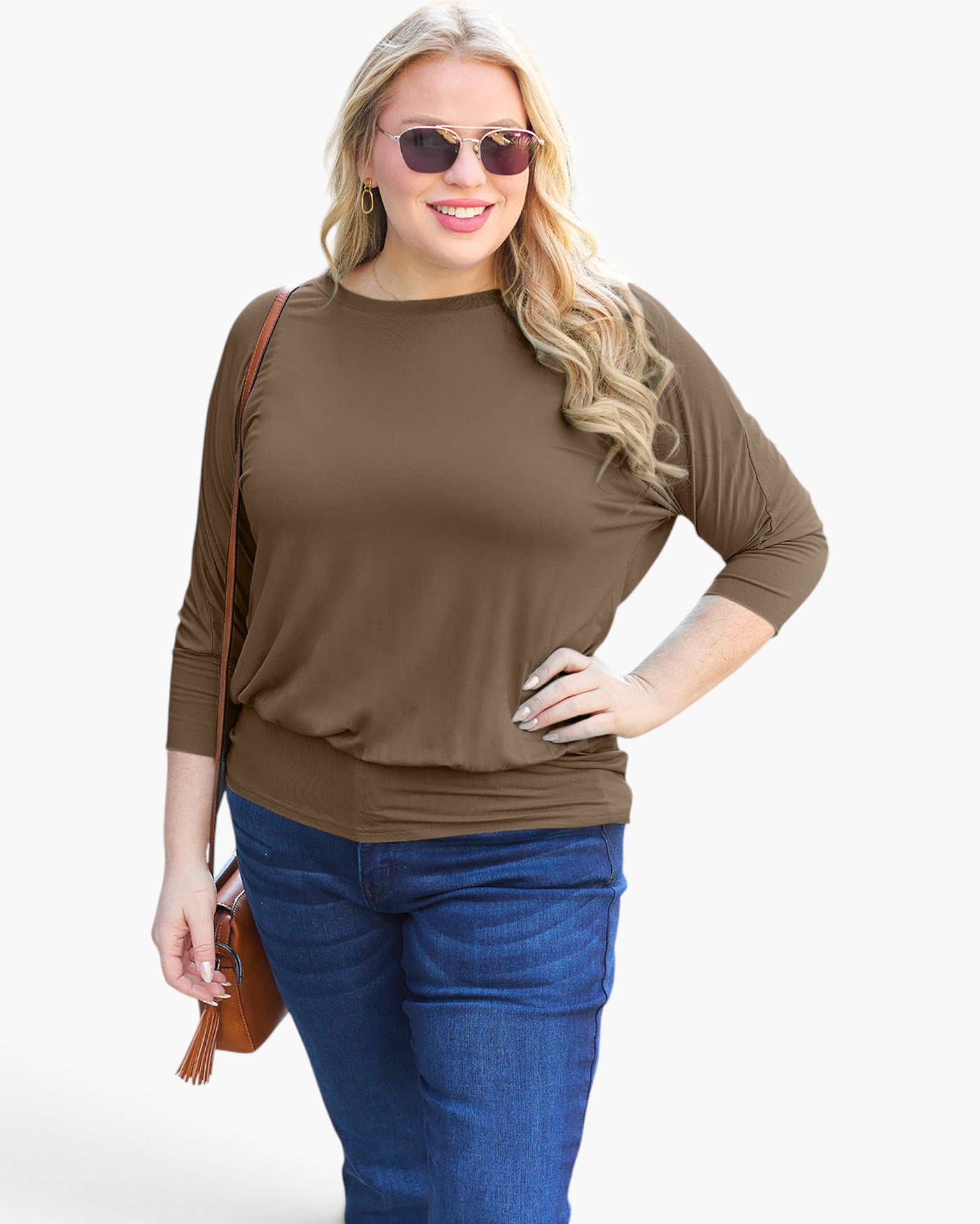 A woman modeling a brown three-quarter sleeve top with blue jeans, sunglasses, and a small brown crossbody bag against a plain white background.
