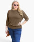 A woman modeling a brown three-quarter sleeve top with blue jeans, sunglasses, and a small brown crossbody bag against a plain white background.