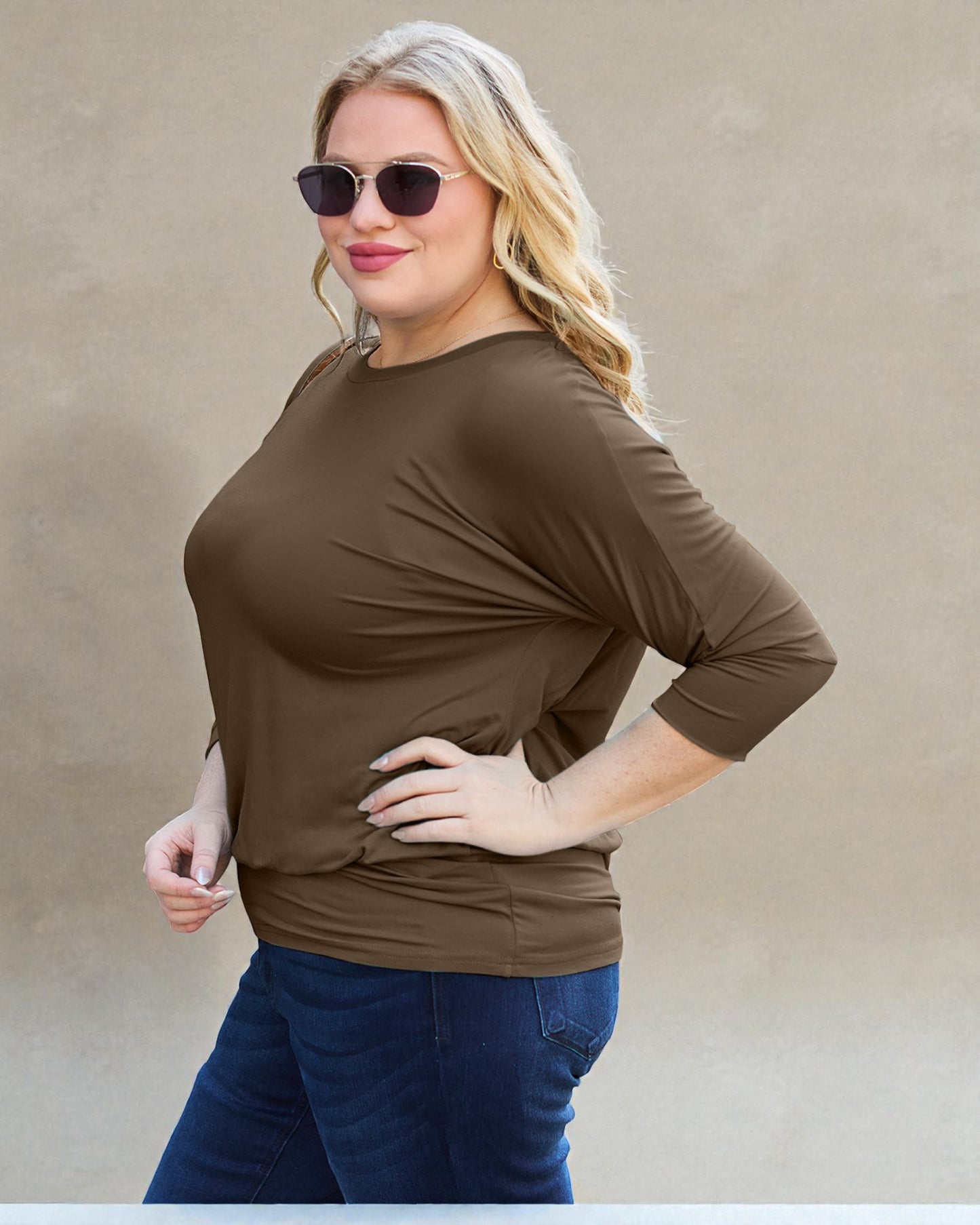 Woman wearing a brown long-sleeve top and blue jeans against a beige background