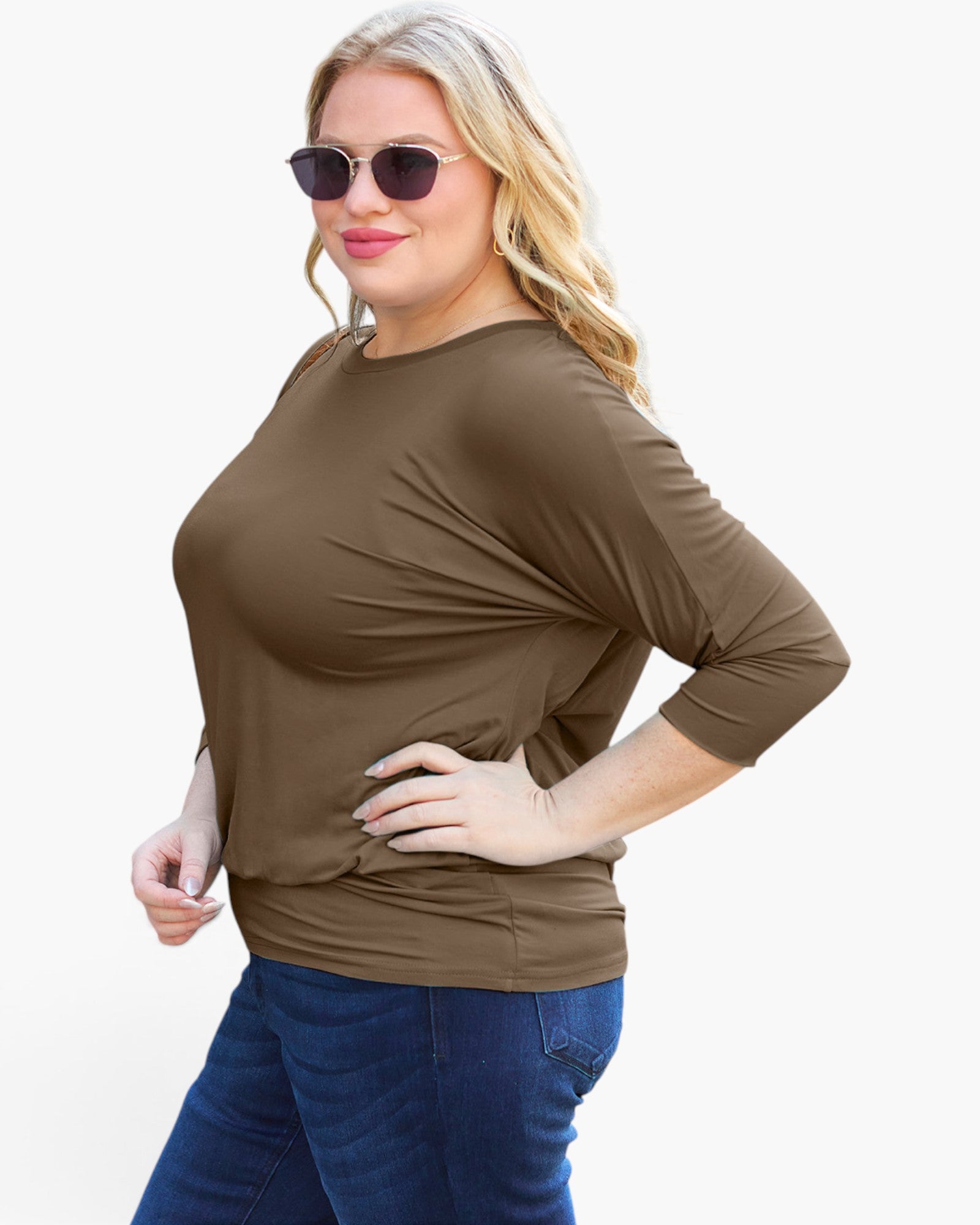 A woman modeling a brown three-quarter sleeve top with a draped, slouchy fit, paired with blue jeans against a plain white background.