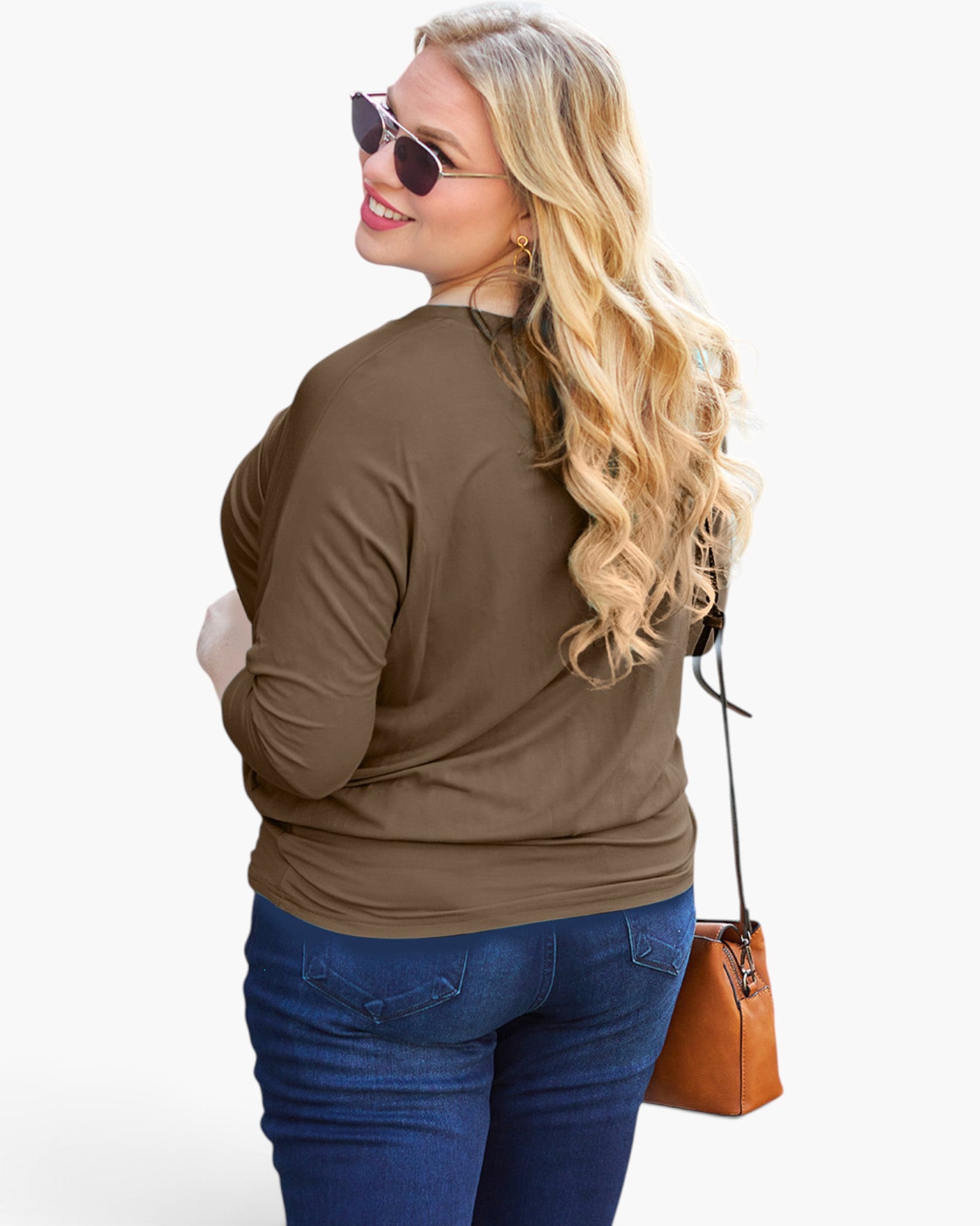 A woman with long blonde wavy hair, wearing sunglasses, a brown long-sleeve top, and blue jeans, shown from a back-three-quarter angle while carrying a brown leather shoulder bag against a white studio background.