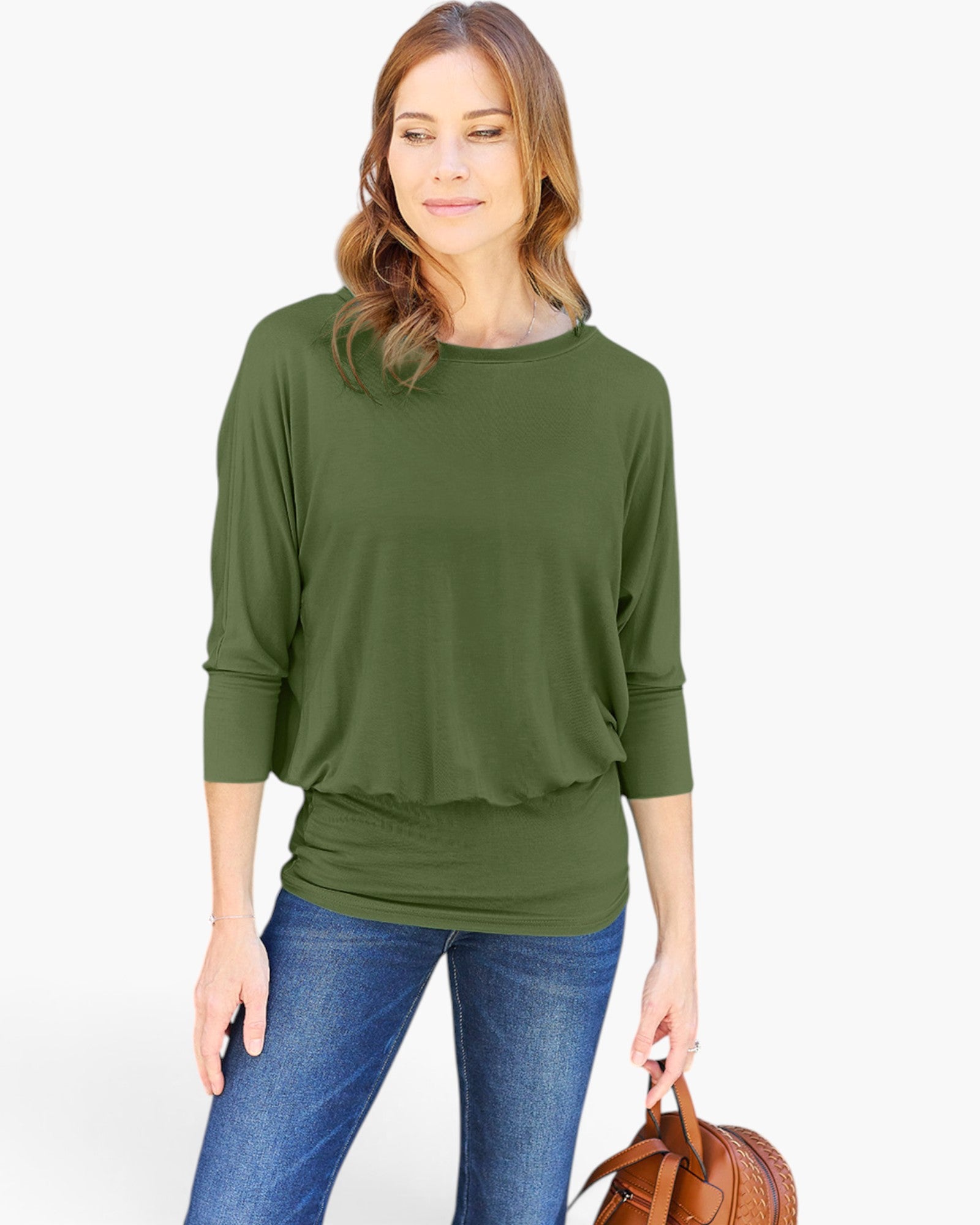 A woman wearing an olive green three-quarter sleeve top with a ruffled hem, paired with blue jeans and holding a brown leather handbag, set against a plain white studio background.