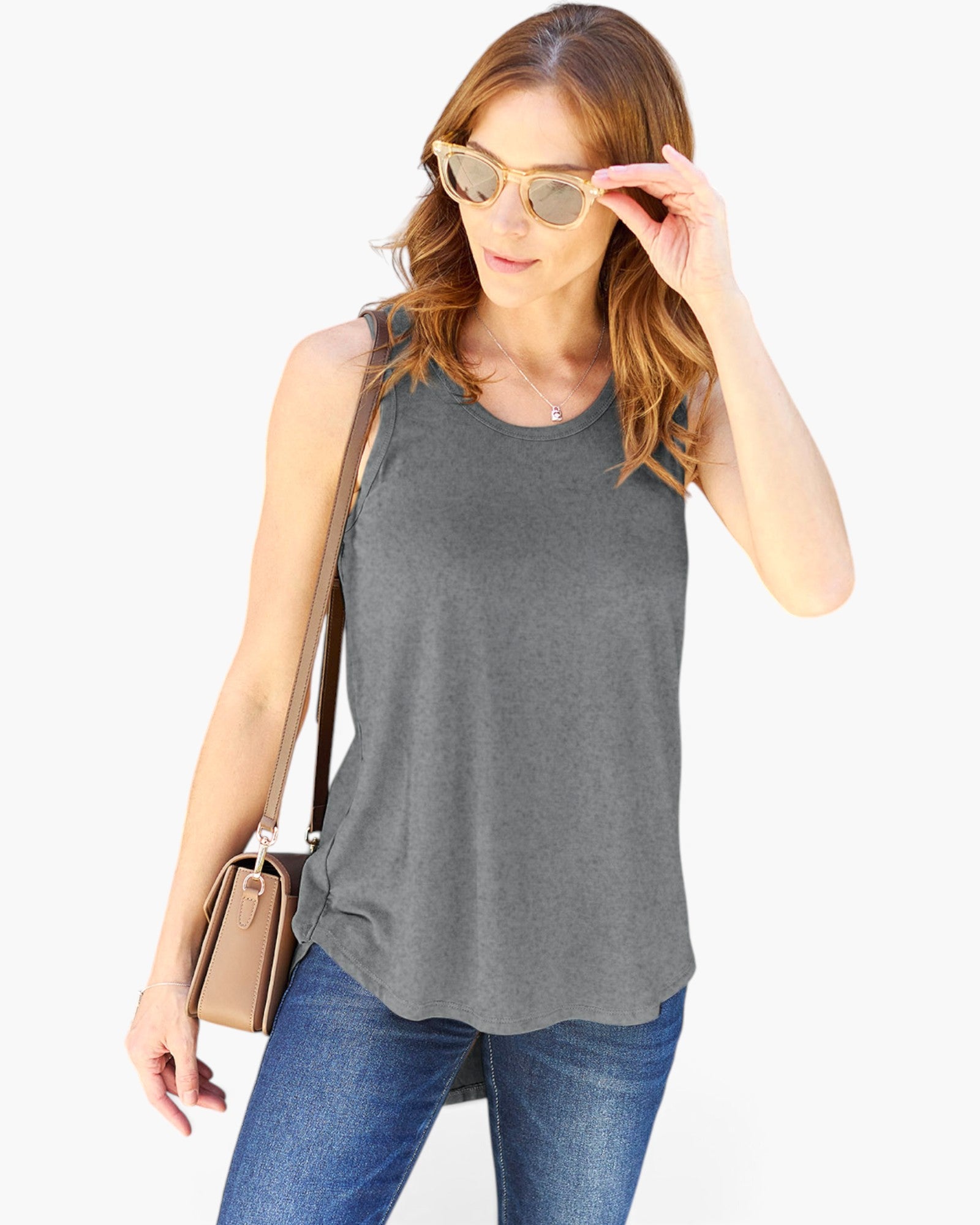 A woman wearing a heather gray sleeveless tank top and blue jeans, accessorized with light gold-framed sunglasses and a tan shoulder bag, against a plain white background.