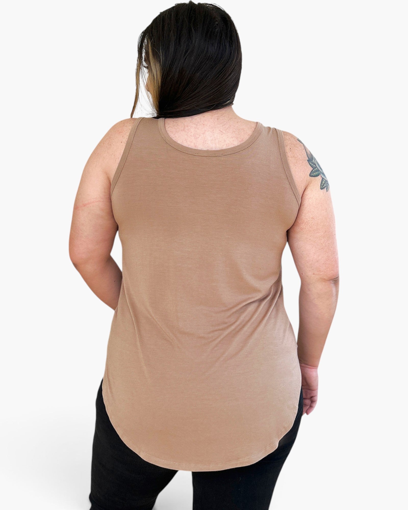 A woman viewed from the back wearing a sleeveless scoop-neck tank top in a warm tan/beige color, paired with black pants, against a plain light gray studio background.