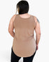 A woman viewed from the back wearing a sleeveless scoop-neck tank top in a warm tan/beige color, paired with black pants, against a plain light gray studio background.