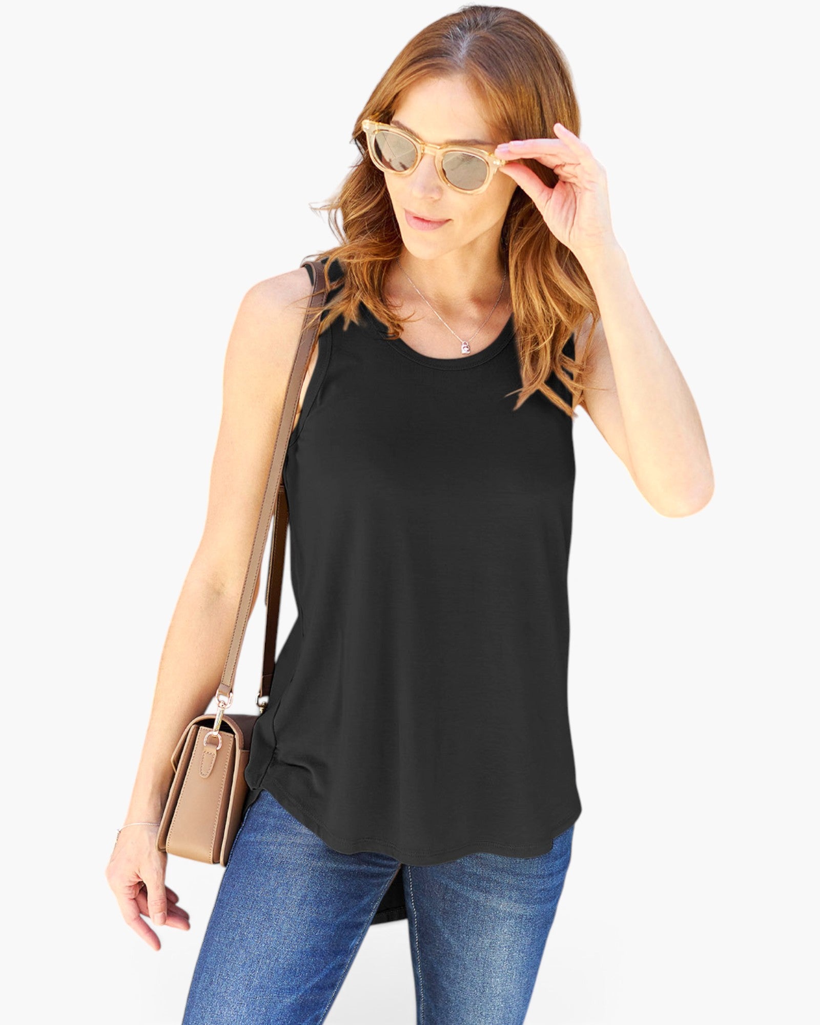 A woman wearing a black sleeveless tank top and blue jeans, accessorized with light gold sunglasses and a tan shoulder bag, set against a plain white background.