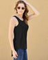 Woman wearing a black sleeveless top and blue jeans against a beige background