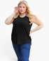 A woman modeling a sleeveless black scoop-neck top with blue jeans against a plain white studio background.
