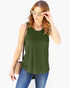 A woman wearing a sleeveless olive green tank top, blue jeans, and light-colored sunglasses, carrying a beige shoulder bag against a plain white background.