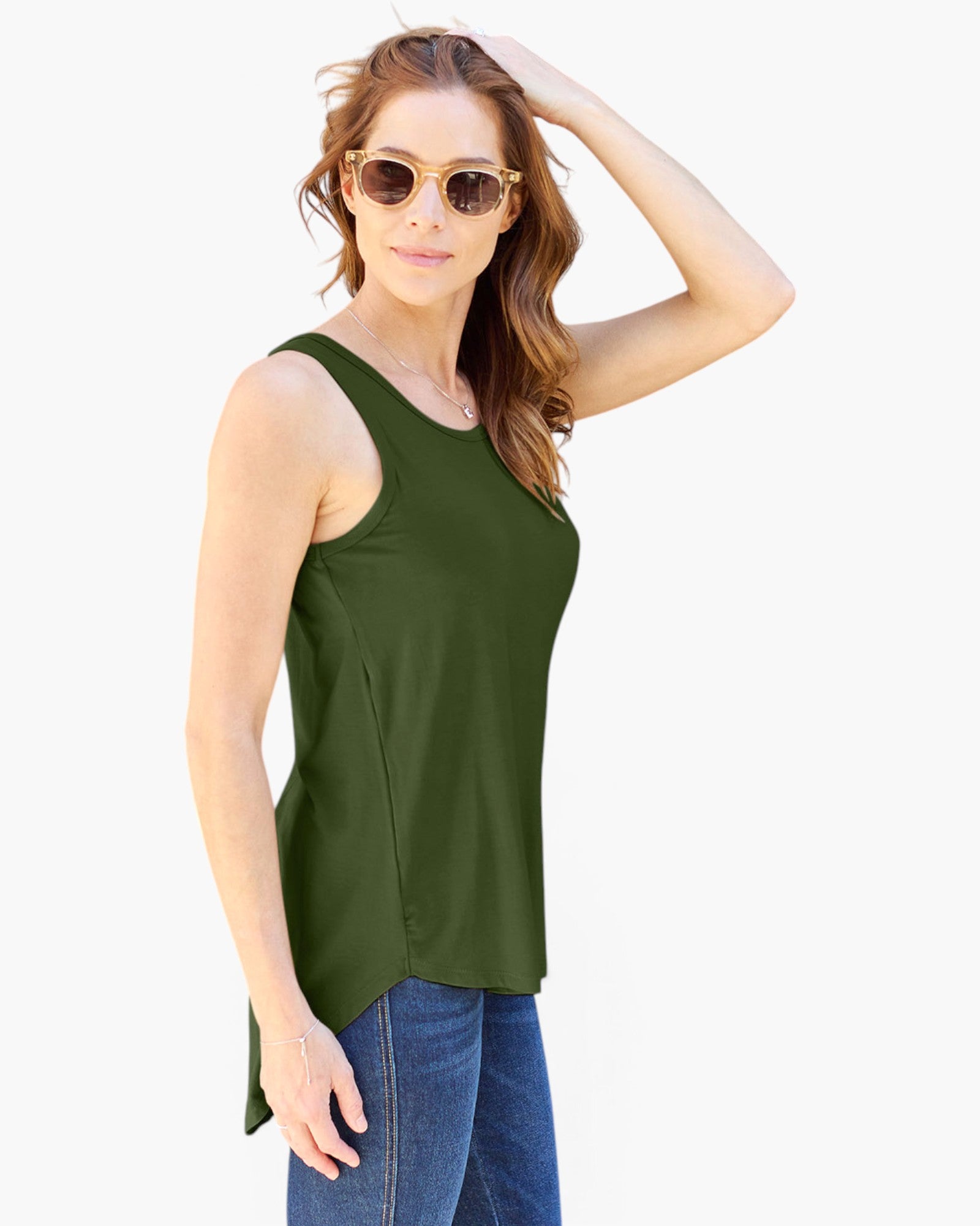 A woman modeling a sleeveless olive green scoop-neck tank top with a high-low hem, paired with blue jeans and round sunglasses, against a plain white background.